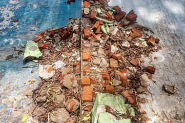 A pile of broken bricks, concrete, and debris on a weathered, blue-painted surface. This image...