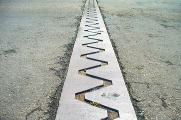 Close up of a bridge expansion joint with a zigzag pattern, designed to accommodate structural movements and prevent damage