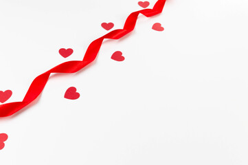 Top view of red ribbon and red hearts on white background. Valentine's day, love. Shiny rolled fabric, silk and satin material. Copy space, flat lay.