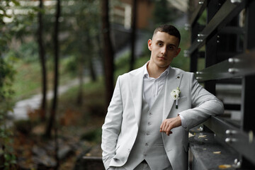 a man dressed in a light gray suit with a vest and white shirt. He has a white flower boutonniere...