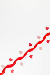 Top view of red ribbon, red hearts and pink glitter hearts on white background. Valentine's day, love. Shiny rolled fabric, silk and satin material. Copy space, flat lay.