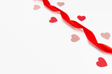 Top view of red ribbon, red hearts and pink glitter hearts on white background. Valentine's day, love. Shiny rolled fabric, silk and satin material. Copy space, flat lay.