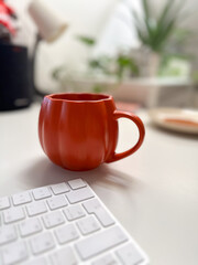 Cozy autumn workspace with a vibrant pumpkin shaped mug on a clean desk. Minimalist decor and warm tones create a relaxing atmosphere, perfect for work or leisure during the fall season