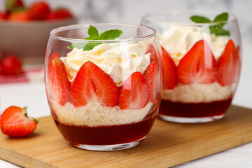 Tasty trifle dessert. Sponge cake, strawberries, jam and whipped cream in glasses on table, closeup