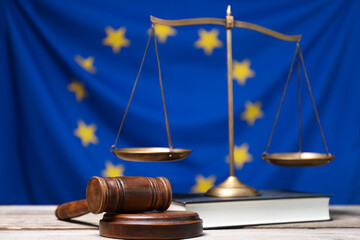 Judge's gavel, scales of justice and book on wooden table against European Union flag