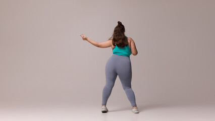 Rear view of plus size woman in blue top and leggings standing with one hand extended outward,...