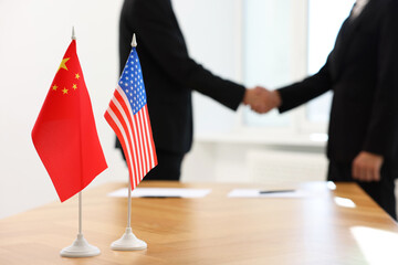 Diplomats shaking hands during meeting indoors, focus on flags of USA and China