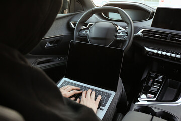 Thief hacking car system with laptop inside vehicle, closeup
