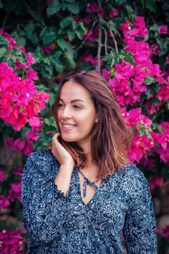 young brunette woman wearing a floral pattern summer dress, next to colorful blooming bushes, on Mallorca