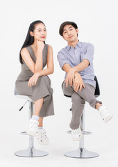 Fototapeta premium Portrait of lovely young asian happy attractive cheerful couple love, Joyful sweethearts enjoy good time romantic date, sitting on stools posing to camera smiling against together on white background.