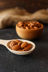 Wooden spoon filled with raw almonds on a rustic dark surface. Scattered almonds create a natural and wholesome ambiance. A burlap background adds warmth and texture to the scene