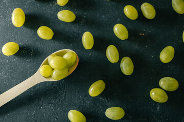 Scattered green grapes and a wooden spoon on a textured dark surface. A simple and rustic...