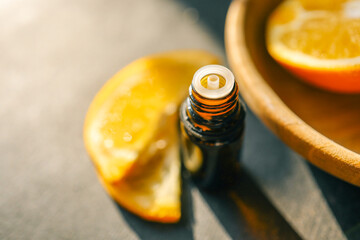 Amber glass bottle with open lid on a dark surface, surrounded by fresh orange slices. The warm sunlight enhances the rich tones, creating a natural and refreshing atmosphere