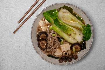 Traditional Japanese Miso soup with Wakame seaweed, tofu cheese, shiitake and enoki mushrooms, soba noodles and pak choi with chopsticks for single serving. Vegetarian, vegan and healthy concept.