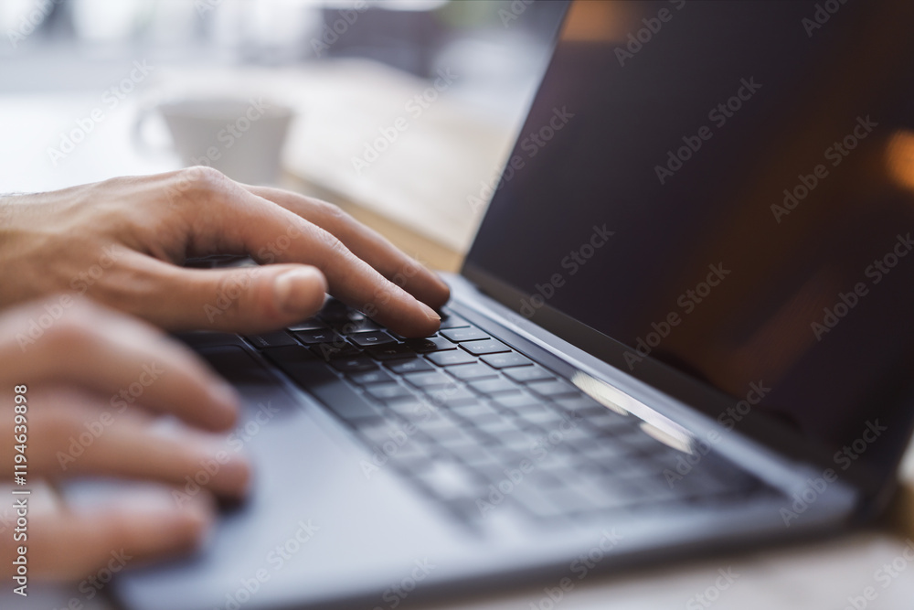 Poster against a fuzzy office backdrop, a close-up captures a man's hands deftly navigating a modern laptop