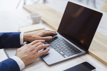 The blurred office scene is the backdrop for a close-up view of a man's hands as they type on a modern laptop.