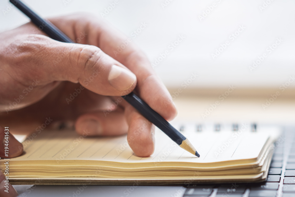 Aufkleber the image highlights a man's hand writing in a notepad on a laptop, with a faintly blurred surroundi
