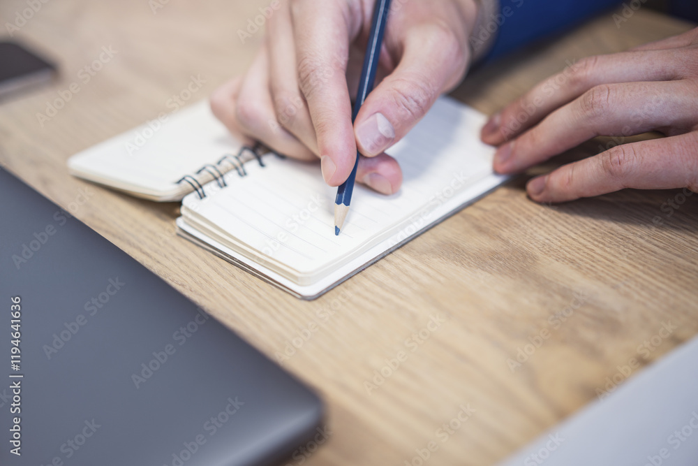 Poster In close view, a man's hand writing down notes in a notepad, against a hazy backdrop