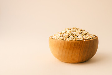 A wooden bowl filled with rolled oats on a beige background. The minimalistic composition highlights the natural texture and color of the oats, emphasizing simplicity and health