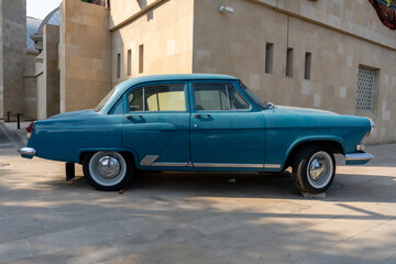 A blue vintage car is parked in front of a building. The car is old and has a classic design. The scene gives off a nostalgic and vintage vibe, as if it's from a bygone era