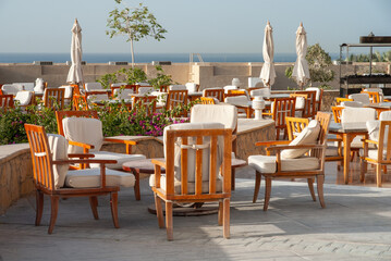 Sharm el Sheikh. Egypt. Open air hotel restaurant. Wooden furniture including tables and armchairs arranged on object overlooking sea. Close-up. An environment of relaxation and enjoyment.