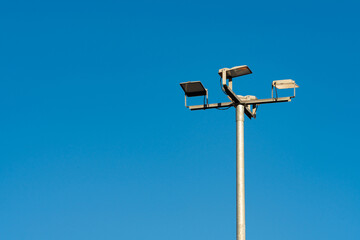 A tall pole supports multiple streetlight fixtures against a bright blue sky. The cloudless...