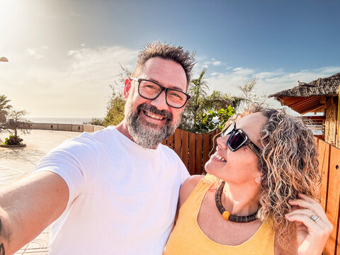 A happy couple taking a selfie on a sandy tropical beach during a sunny summer vacation, with golden sand, blue ocean waves, and a bright, clear sky creating a picturesque and relaxing setting