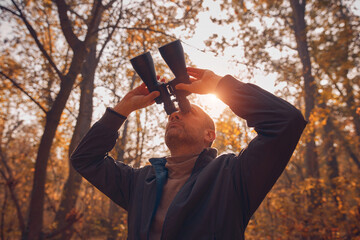 Amateur birdwatcher observing birds and other animals in nature with binoculars.