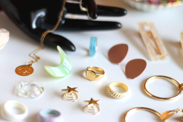 Hand figurine, sunglasses, gold jewelry, colorful bead jewelry, statement rings and various hair accessories on the white table. Selective focus.