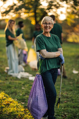 Smiling senior volunteer posing while picking up trash in park