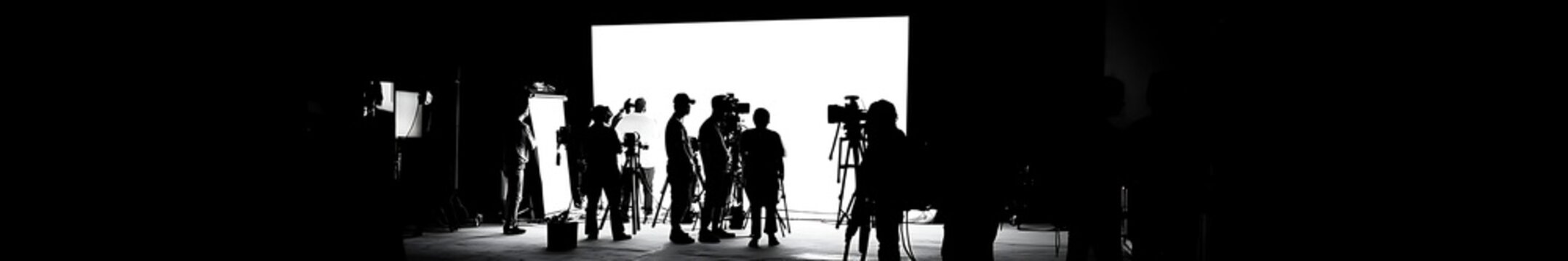 Silhouette of film crew team working behind the scenes in a professional studio for video production, featuring director, cameraman, and lightman collaborating on TV commercial movie making 