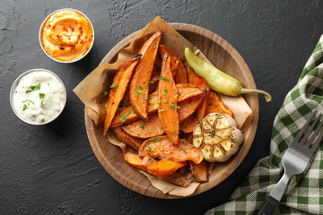 Tasty cooked sweet potatoes with garlic, pickled pepper and sauces on black table, top view