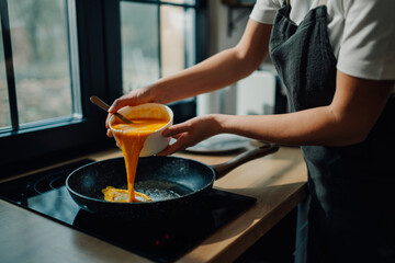 Chef pouring scrambled eggs mixture into frying pan in kitchen