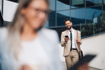 Businessman walking and using phone with colleague in foreground