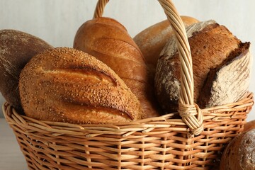 Different freshly baked bread loafs in wicker basket on table, closeup