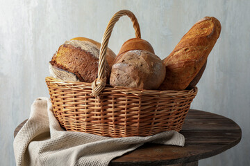Different freshly baked bread loafs in wicker basket on wooden table, closeup