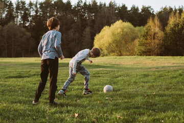 Two teenage friends, classmates, brothers play football in park, in nature on autumn evening.