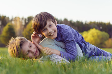Portrait of two happy laughing teenage boys, friends, brothers lying on green grass of lawn.