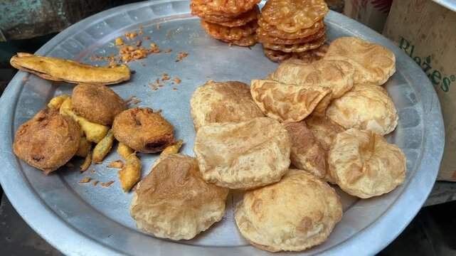 Freshly prepared kachoris, jalebis and pakoras and tele bhaja on aluminium tray at display in shop.