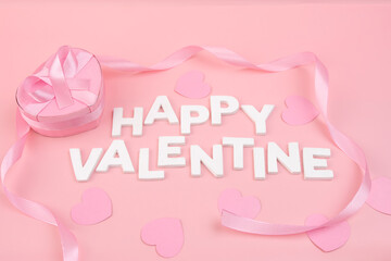 A heart shaped box with a pink ribbon is next to the words Happy Valentine spelled out in white letters. valentine concept background