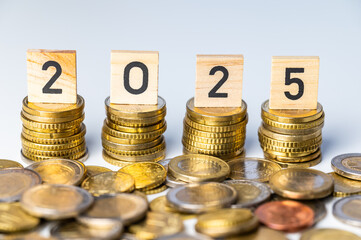 Piles of coins, and wooden cubes that spell out the number 2025. New year, economy and wealth.
