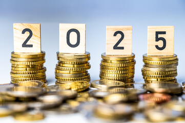 Piles of coins, and wooden cubes that spell out the number 2025. New year, economy and wealth.

