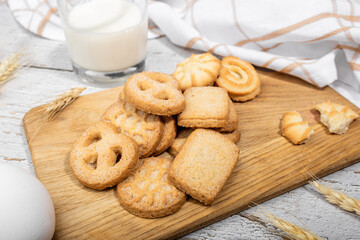 Danish cookies on a wooden background in a rustic cozy style with a glass of milk, wheat ears, a white towel on the table, eggs, making cookies, shortbread cookies with milk
