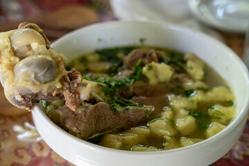 A bowl of soup with a piece of meat in it. The soup is green and has a lot of vegetables in it
