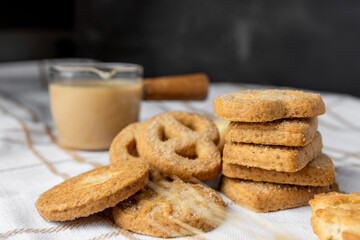 Danish shortbread cookies on a white towel, boiled condensed milk in a glass milk jug, light still life, wheat ears, tea with cookies