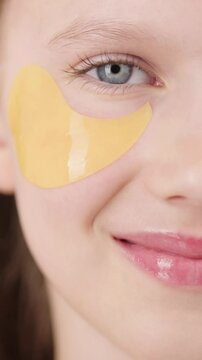 VERTICAL VIDEO. Happy cute young girl with eye patch in studio. Half-face portrait of pretty blonde girl gen Alpha smiling looking at the camera. Concept of cosmetics advertisement for teenagers.
