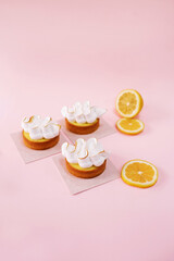 Lemon tarts covered with white meringue isolated on the pink background with sliced ​​lemon