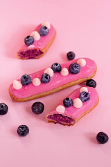 eclairs decorated with pink cream and blueberries isolated on pink background