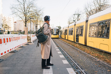 Businesswoman waiting for the tram wearing headphones and backpack at the station 