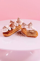 eclair decorated with white cream and cocoa cut in half on a white plate